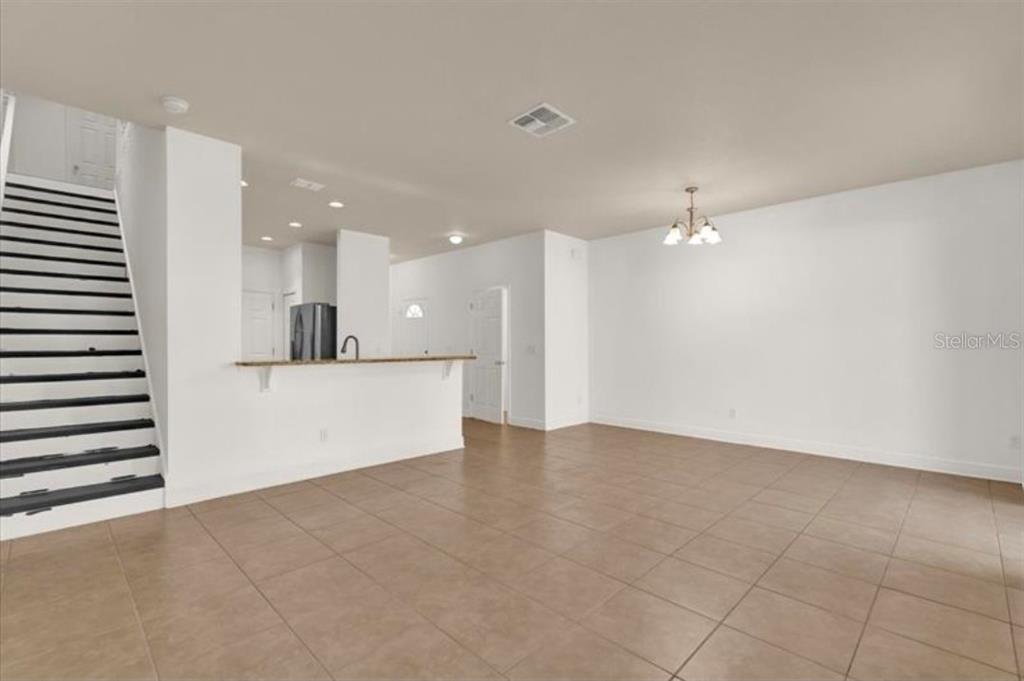 An empty room with beige tile flooring, white walls, a chandelier, and a sliding glass door — 9301 WATCHET WAY, ORLANDO, FL