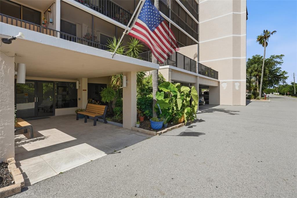 An exterior view of a building entrance with a covered patio, benches, and American flag — 25188 MARION AVE UNIT D307, PUNTA GORDA, FL