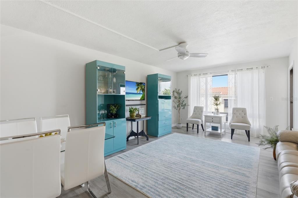 A bright living and dining room features light flooring, teal cabinets, and white furniture — 25188 MARION AVE UNIT D307, PUNTA GORDA, FL
