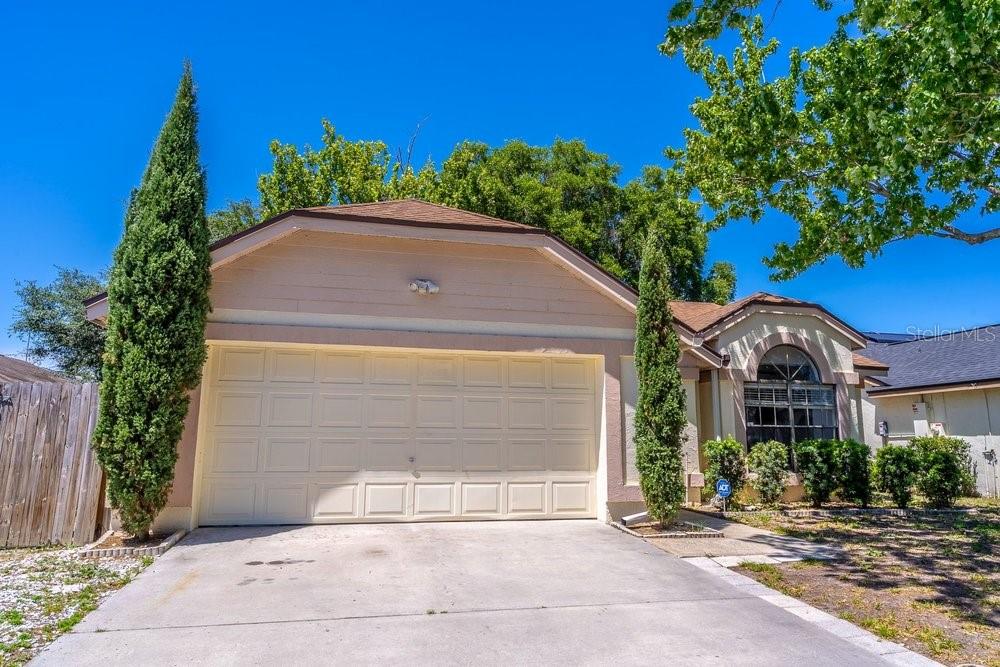 A beige house with a two-car garage and two tall cypress trees in the front — 1345 TINDARO DRIVE, APOPKA, FL