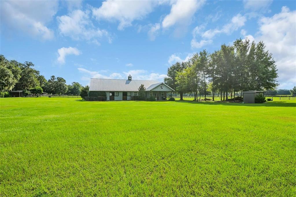A large metal-roofed barn sits in the middle of a vast, open green pasture — 6155 NW 145TH AVE ROAD, MORRISTON, FL