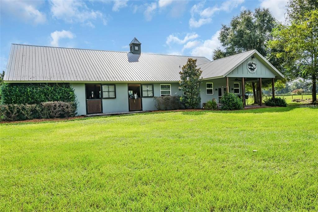 A light-colored horse barn with a metal roof and a covered porch on a lawn — 6155 NW 145TH AVE ROAD, MORRISTON, FL