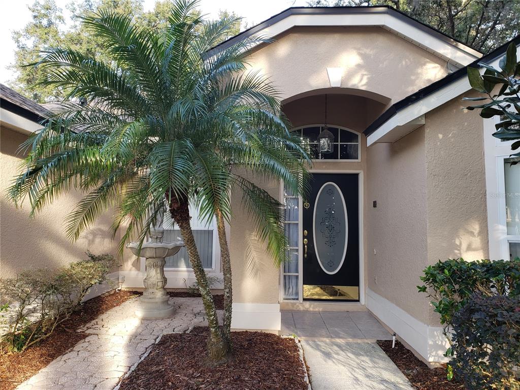 A tan house exterior features a black front door, a palm tree, and a stone fountain — 1612 SWEETWATER WEST CIRCLE, APOPKA, FL