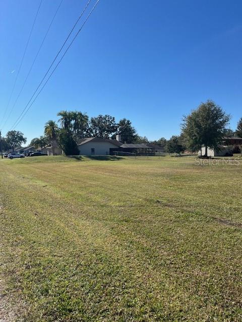 A large, flat, grassy vacant lot sits in front of a suburban house and trees — Lot 589 MARIE DRIVE, ZEPHYRHILLS, FL