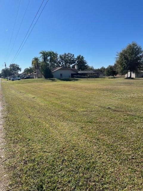 A large, grassy vacant lot is shown with a house and trees in the background — Lot 589 MARIE DRIVE, ZEPHYRHILLS, FL