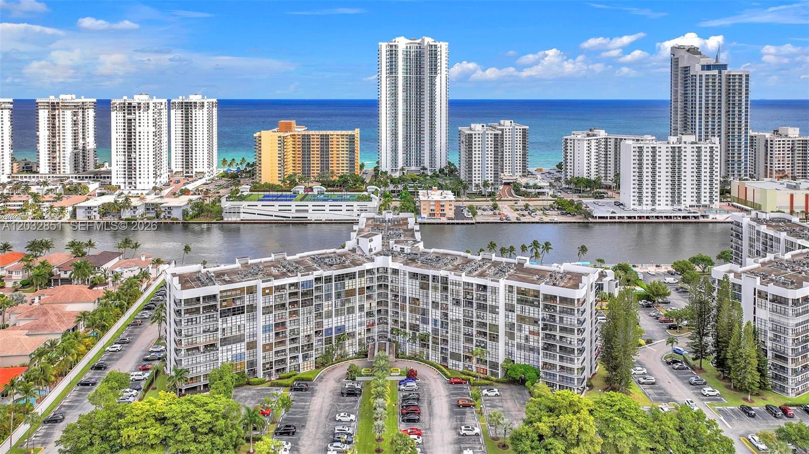 An aerial view shows a multi-story residential building with a parking lot and waterfront — 1000 Parkview Dr # 229, Hallandale Beach FL 33009, HALLANDALE BEACH, FL
