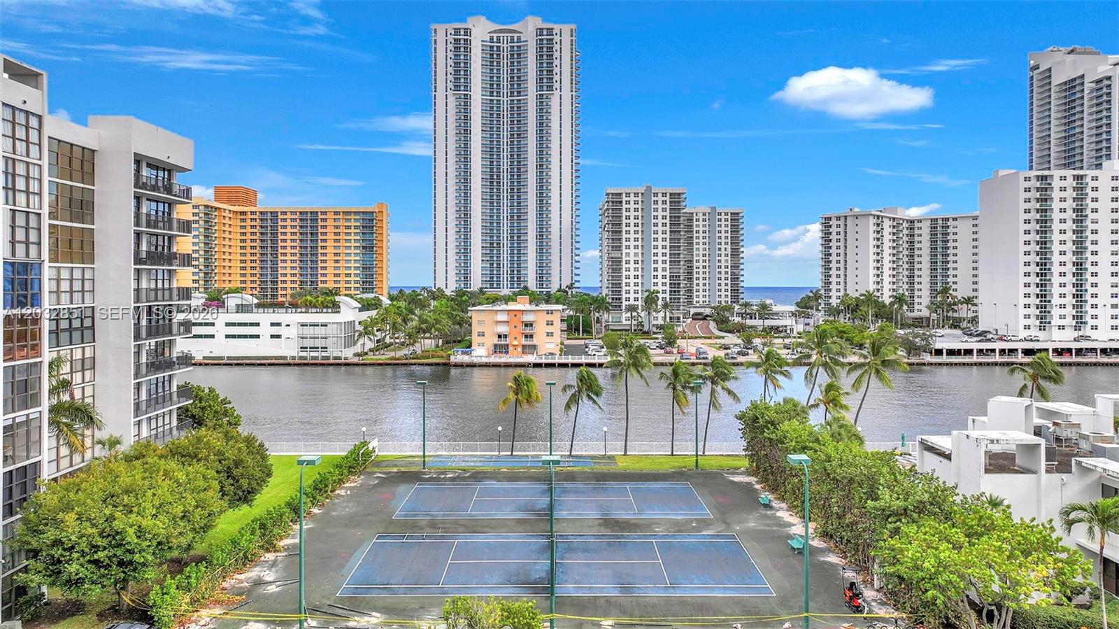 An outdoor tennis court sits in the foreground before a canal and high-rise buildings — 1000 Parkview Dr # 229, Hallandale Beach FL 33009, HALLANDALE BEACH, FL