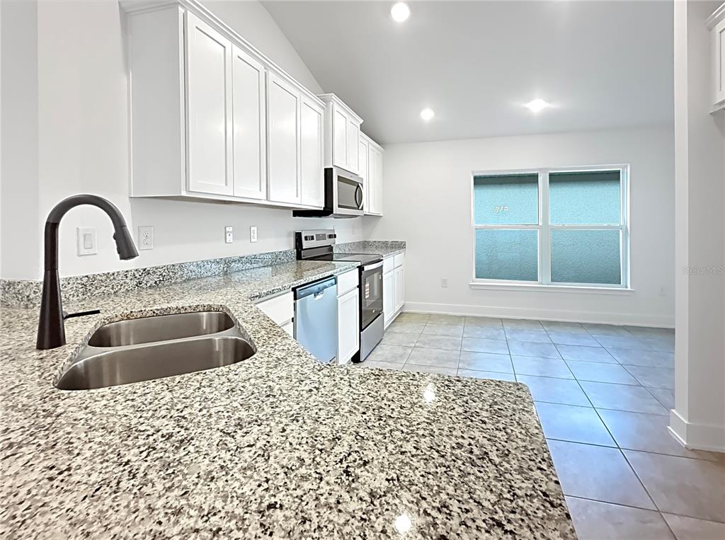 A kitchen features white cabinets, granite countertops, stainless steel appliances, and tile flooring — 7648 BENT TREE LOOP, ST CLOUD, FL