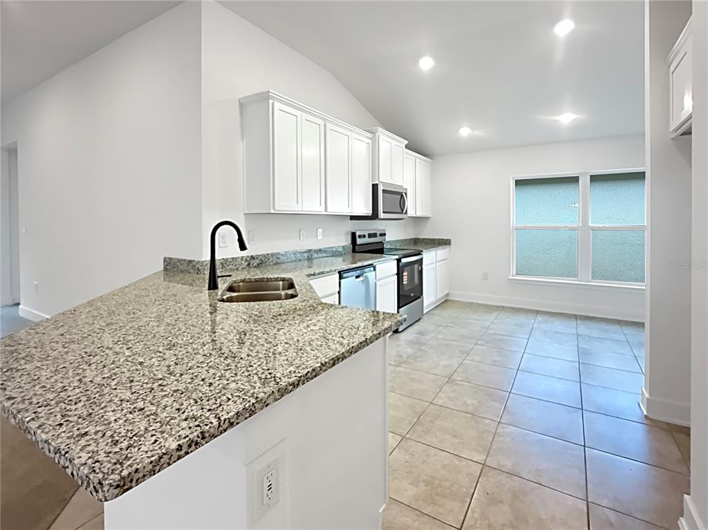 A kitchen features white cabinets, granite countertops, a black faucet, and light-colored tile flooring — 7648 BENT TREE LOOP, ST CLOUD, FL