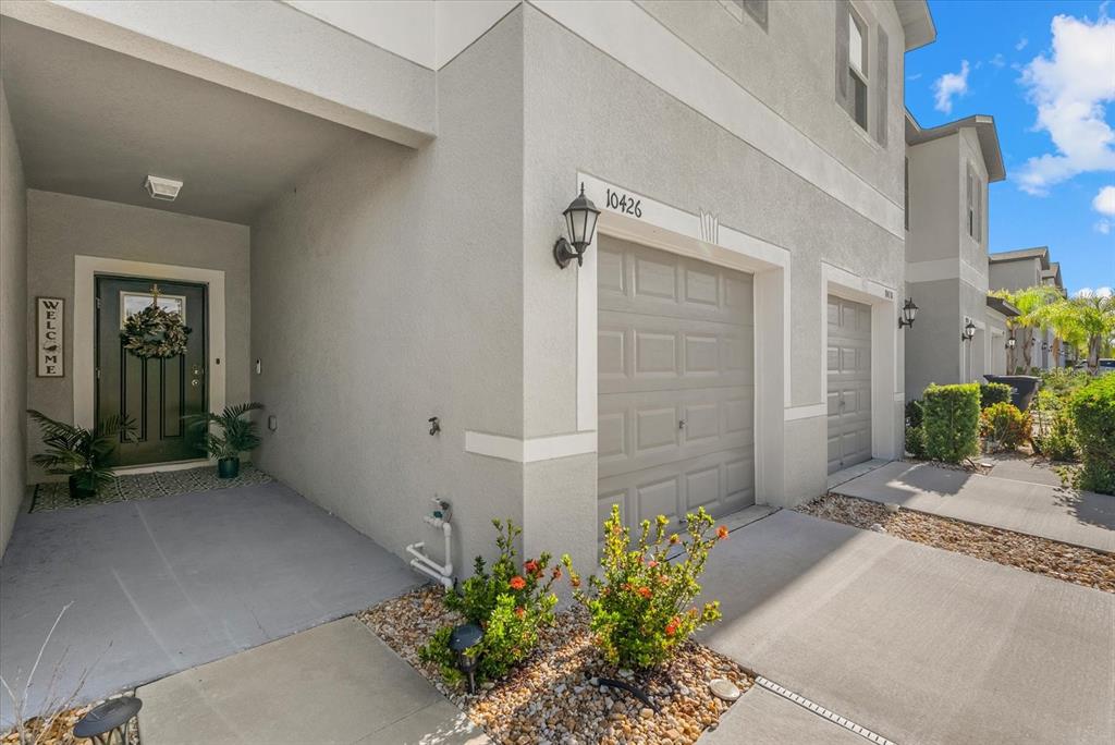 The exterior of a two-story townhouse features a gray garage, a covered entryway, and landscaping — 10426 SHADY PRESERVE DRIVE, RIVERVIEW, FL