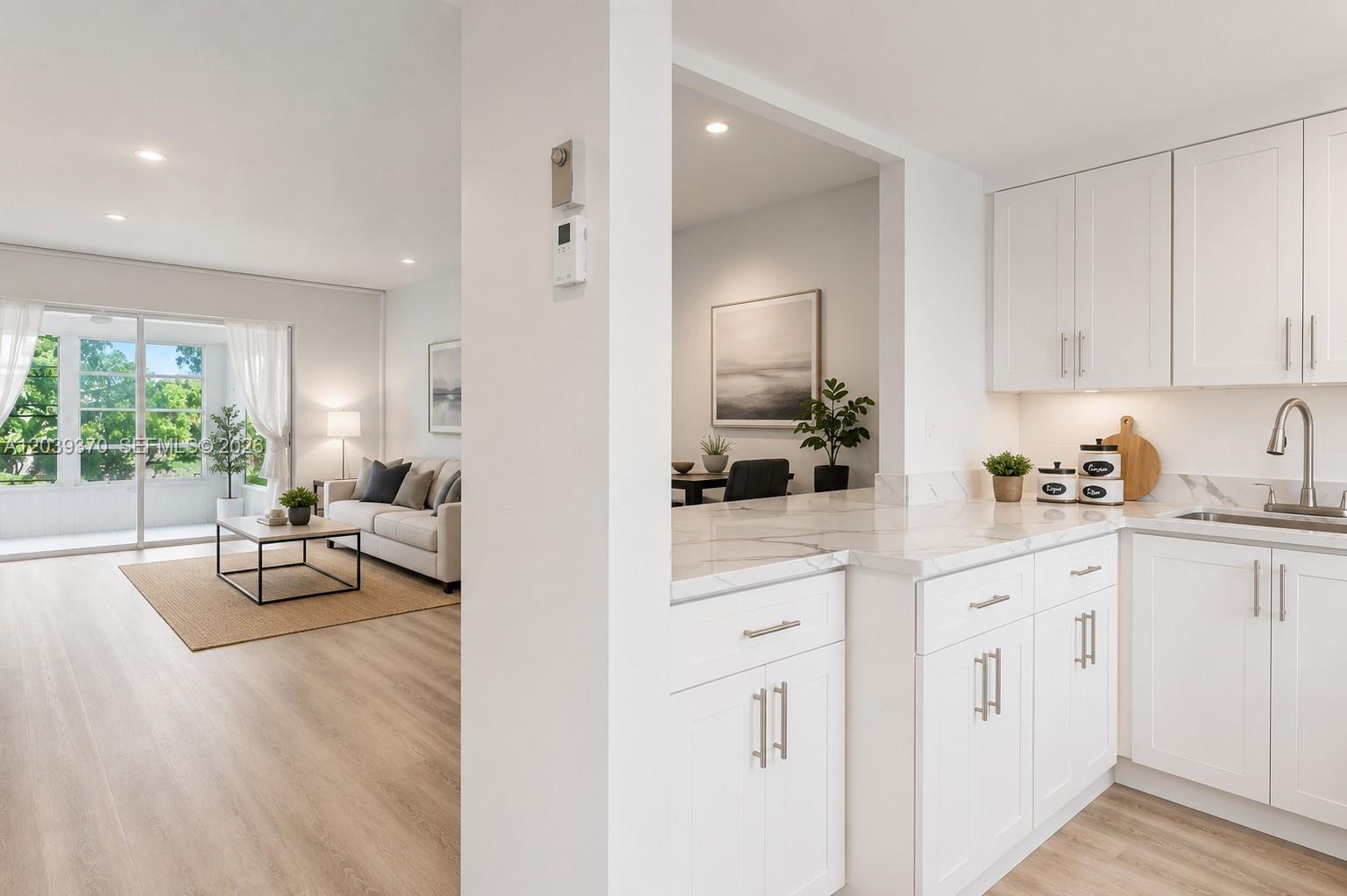 A bright kitchen with white cabinets and marble countertops overlooks a living room and balcony — 7605 NW 5th Pl # 103, Margate FL 33063, MARGATE, FL