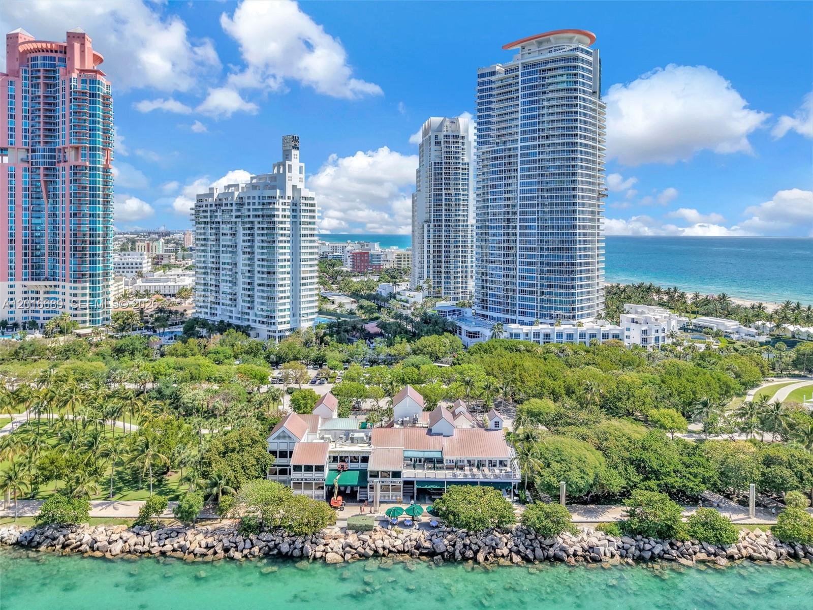 An aerial view shows a waterfront restaurant surrounded by trees in front of tall skyscrapers — 100 S Pointe Dr # 801, Miami Beach FL 33139, MIAMI BEACH, FL