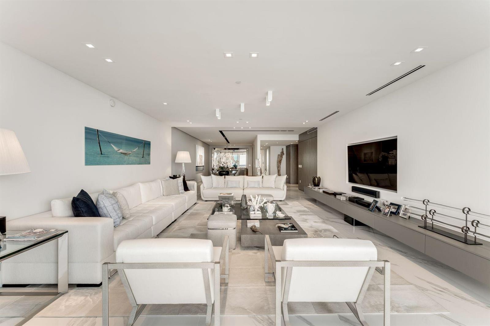 A modern, minimalist living room features white sofas, a glass coffee table, and marble floors — 10201 Collins Avenue # 1803, Bal Harbour FL 33154, BAL HARBOUR, FL