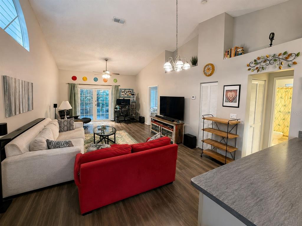 A living room features a white sofa, a red sofa, wood-look flooring, and vaulted ceilings — 2390 GUN FLINT TRAIL, PALM HARBOR, FL