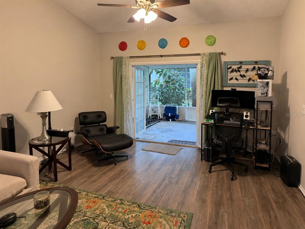 A living room features wood-look flooring, a lounge chair, a desk, and sliding glass doors — 2390 GUN FLINT TRAIL, PALM HARBOR, FL