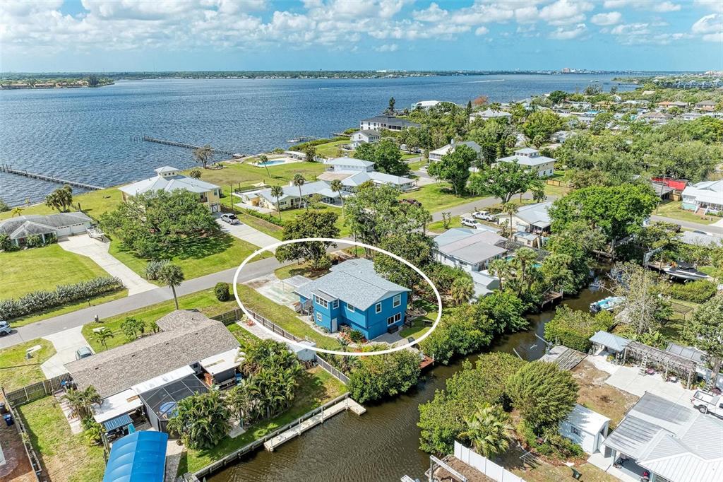 An aerial view shows a blue house with a gray roof situated near a canal — 4518 7TH STREET COURT E, ELLENTON, FL