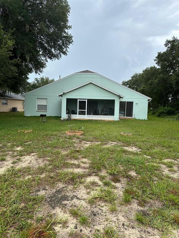 The back exterior of a light green house features a screened-in porch and a yard — 441 CARDINAL COURT, POINCIANA, FL