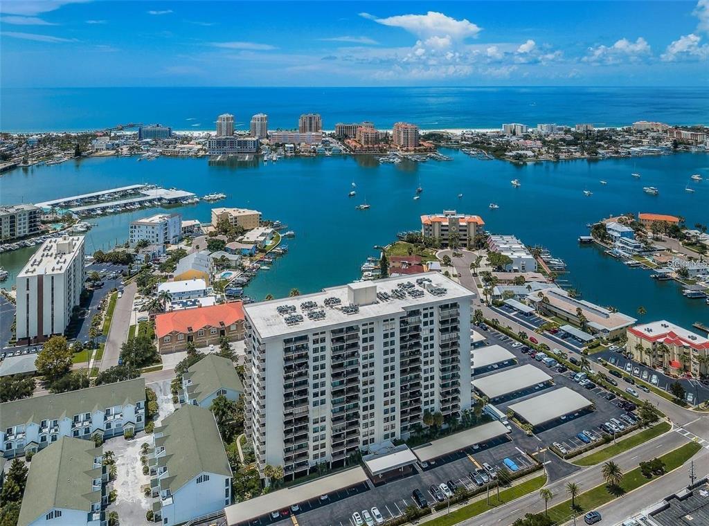An aerial view of a high-rise condominium building surrounded by water, boats, and coastal buildings — 400 ISLAND WAY UNIT 309, CLEARWATER BEACH, FL