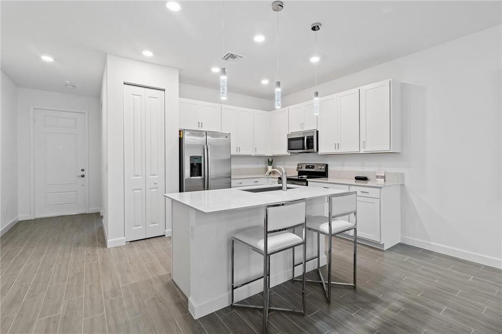 A modern kitchen features white cabinetry, stainless steel appliances, a center island, and gray flooring — 14534 Highland Center Way, Delray Beach FL 33446, DELRAY BEACH, FL