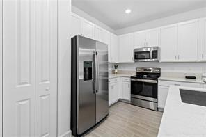 A kitchen features white cabinets, stainless steel appliances, and light-colored flooring — 14534 Highland Center Way, Delray Beach FL 33446, DELRAY BEACH, FL