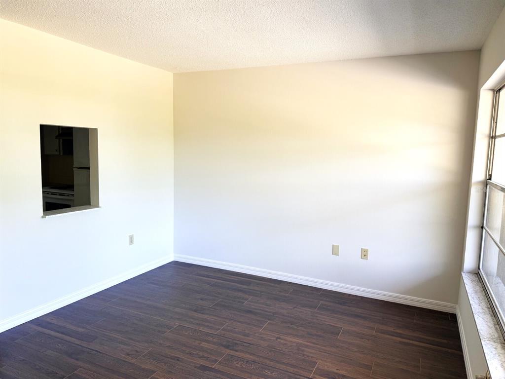 An empty room with dark wood-look flooring, white walls, and a kitchen pass-through window — 2 QUAILS RUN BOULEVARD UNIT 8, ENGLEWOOD, FL