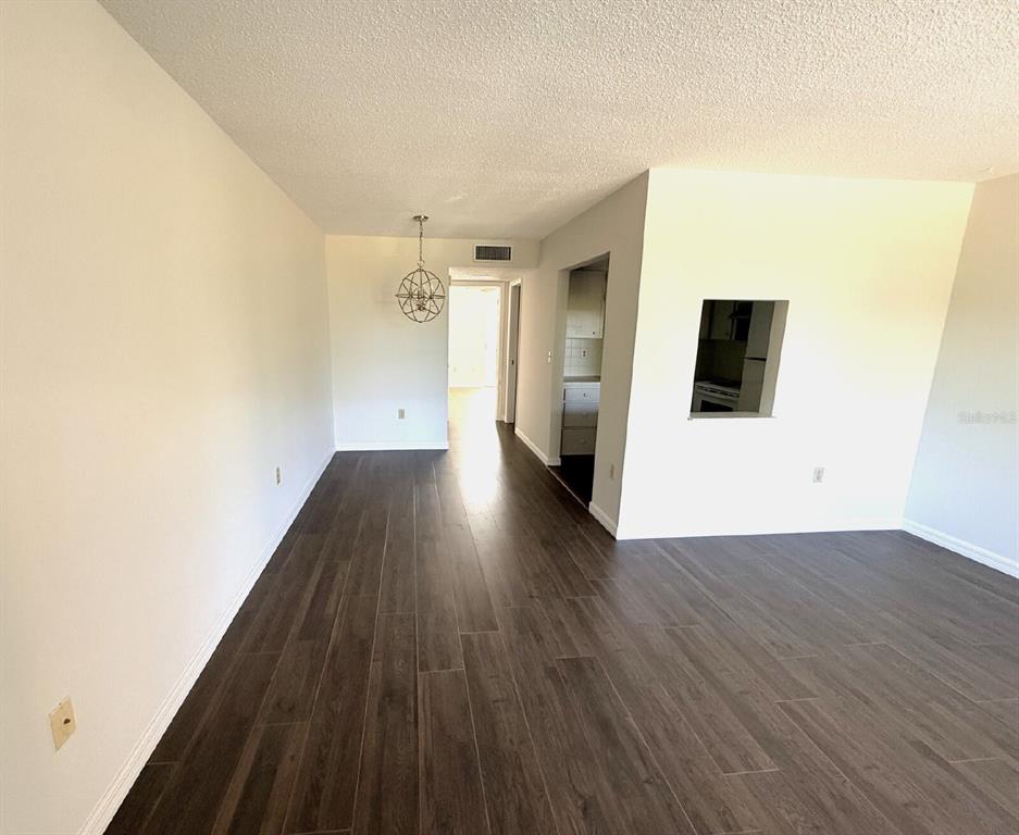An empty room with dark wood-look flooring, white walls, and a hanging light fixture — 2 QUAILS RUN BOULEVARD UNIT 8, ENGLEWOOD, FL