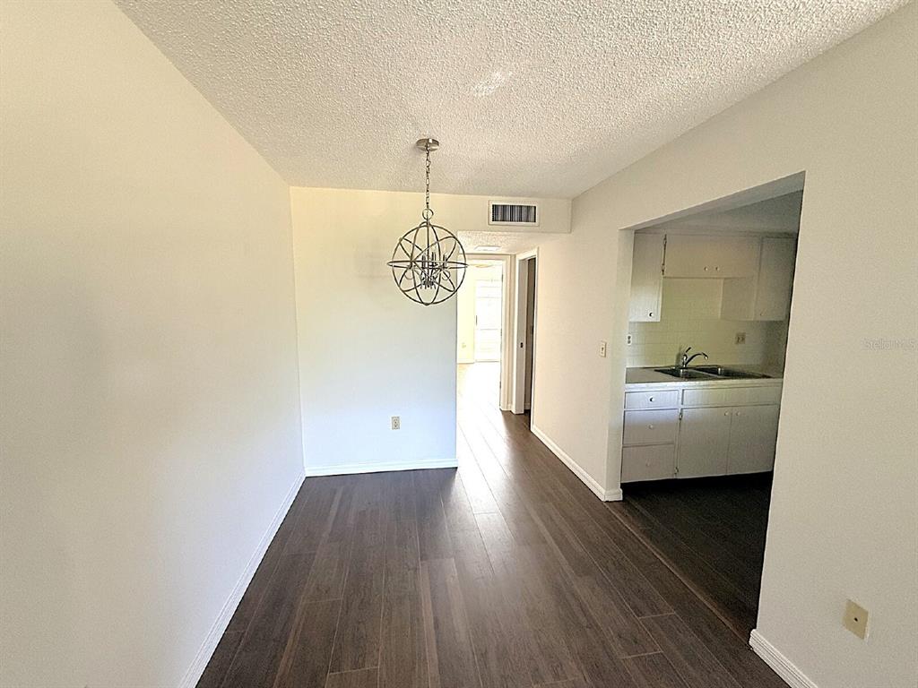 A dining area with dark wood-look flooring, a spherical chandelier, and an adjacent kitchen — 2 QUAILS RUN BOULEVARD UNIT 8, ENGLEWOOD, FL