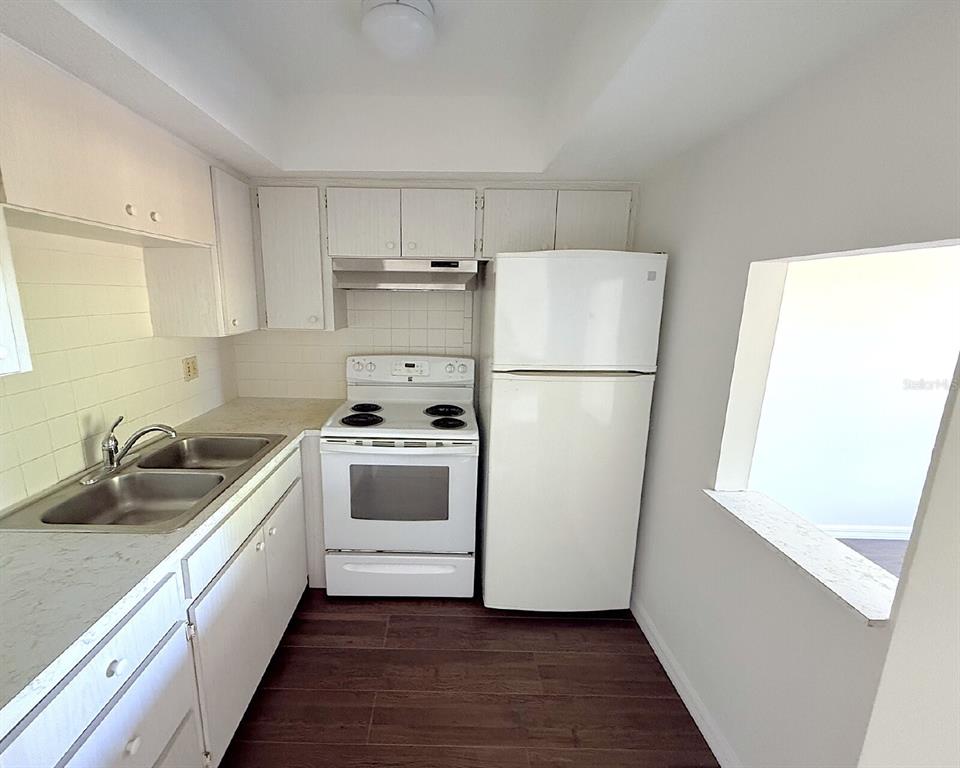 A small kitchen features white cabinets, white appliances, a double sink, and dark wood-look flooring — 2 QUAILS RUN BOULEVARD UNIT 8, ENGLEWOOD, FL