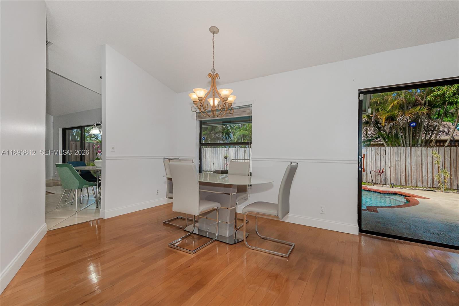 A dining room features hardwood floors, a chandelier, and a sliding door to a pool — 1855 NW 106th Ter, Plantation FL 33322, PLANTATION, FL