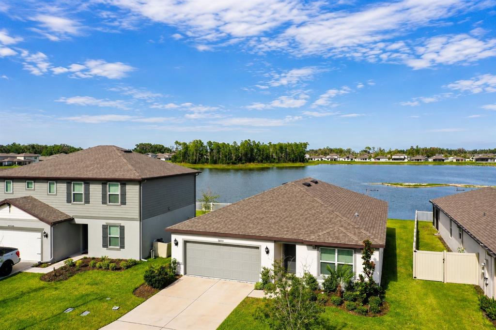 An aerial view shows two suburban houses situated next to a lake under a blue sky — 3830 CAPRI COAST DRIVE, PLANT CITY, FL