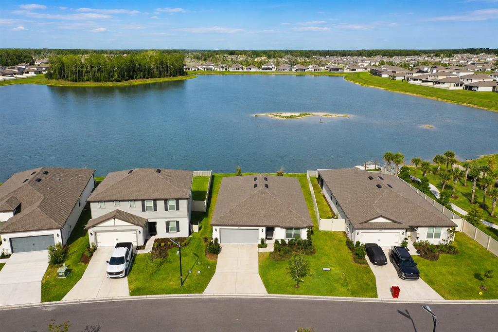An aerial view shows three suburban houses with driveways facing a large lake — 3830 CAPRI COAST DRIVE, PLANT CITY, FL
