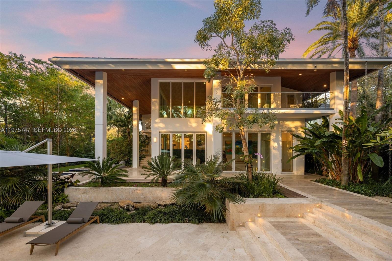 A modern two-story house with a flat roof, glass walls, and a stone patio — 7150 W Lago Dr, Coral Gables FL 33143, CORAL GABLES, FL