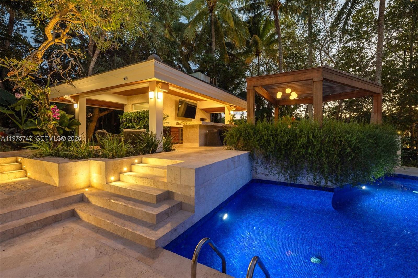 A stone patio with steps leads to a covered outdoor kitchen and a swimming pool — 7150 W Lago Dr, Coral Gables FL 33143, CORAL GABLES, FL