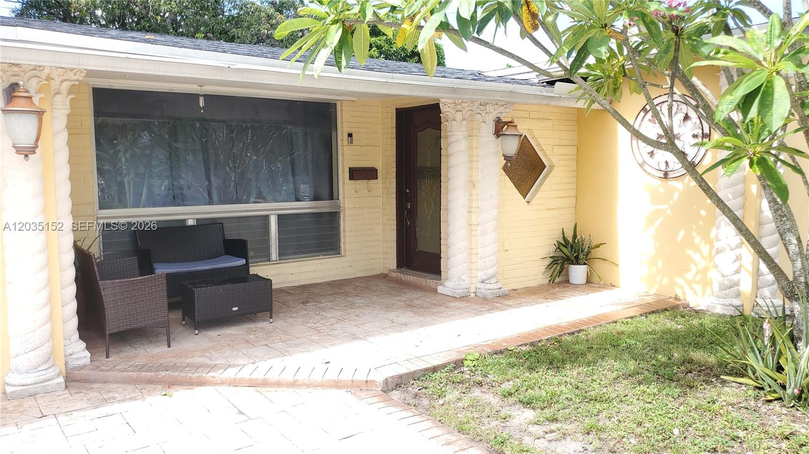 A yellow brick house exterior features a covered patio with columns and wicker furniture — 7607 Dilido Blvd, Miramar FL 33023, MIRAMAR, FL