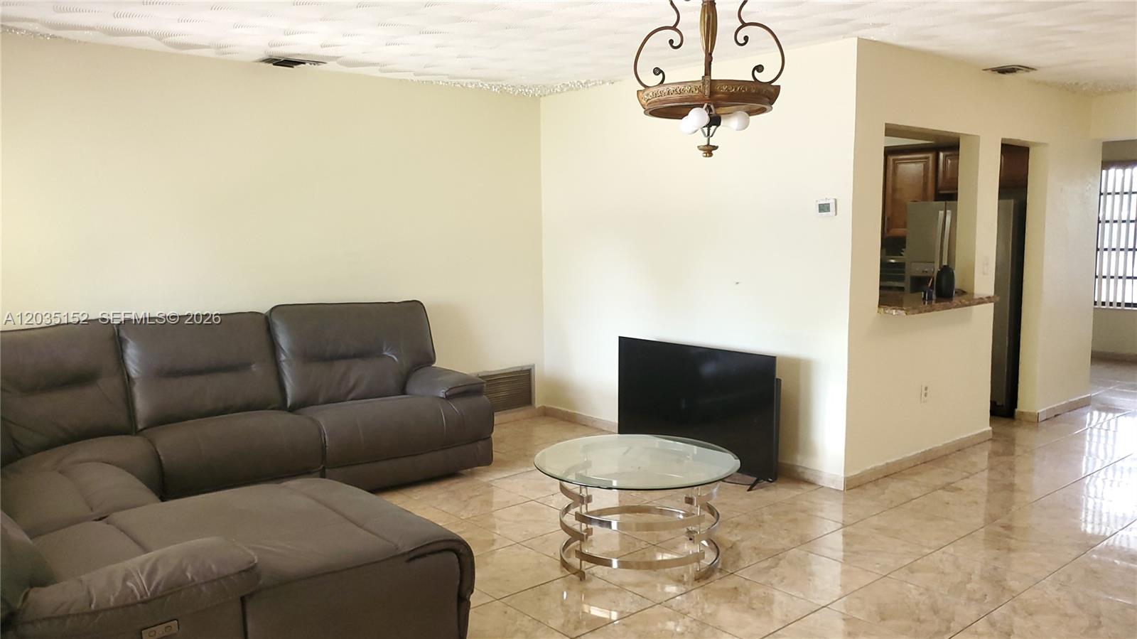 A living room features a grey sectional sofa, a glass coffee table, and tile flooring — 7607 Dilido Blvd, Miramar FL 33023, MIRAMAR, FL