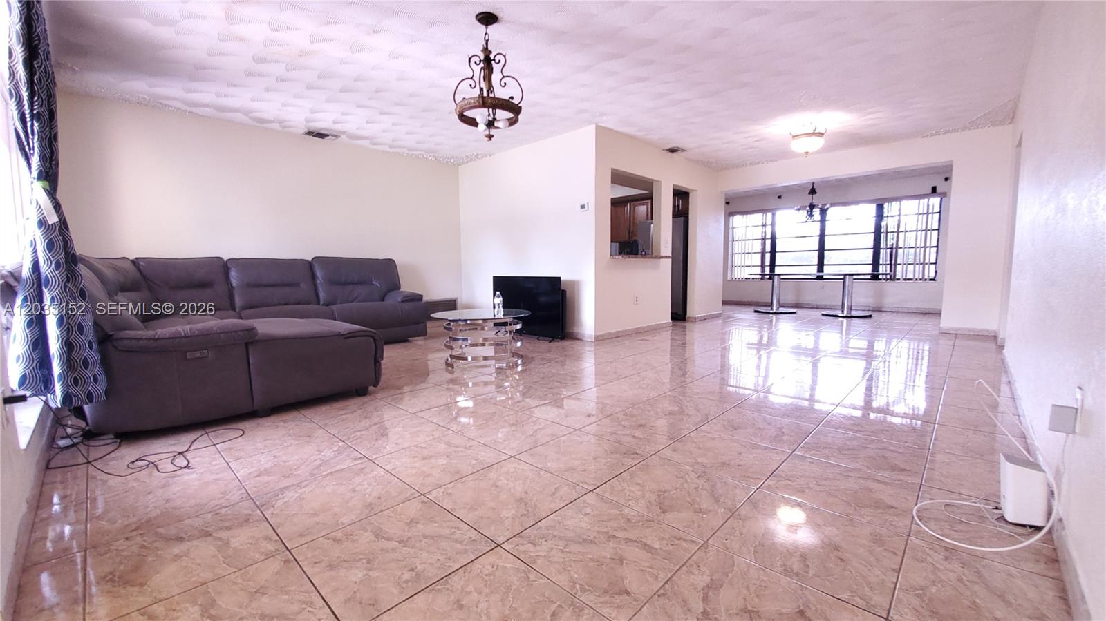 A spacious living room features light-colored tile flooring, a gray sectional sofa, and recessed lighting — 7607 Dilido Blvd, Miramar FL 33023, MIRAMAR, FL