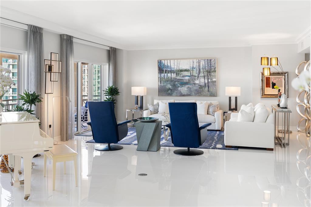 A bright living room features white tile floors, two blue armchairs, and a white piano — 1111 RITZ CARLTON DRIVE UNIT 1603, SARASOTA, FL