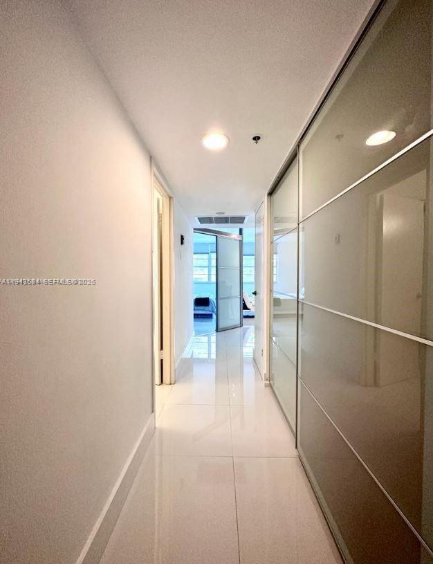 A bright hallway features white tiled floors, plain walls, and a large sliding glass closet — 100 Lincoln Rd # 526, Miami Beach FL 33139, MIAMI BEACH, FL
