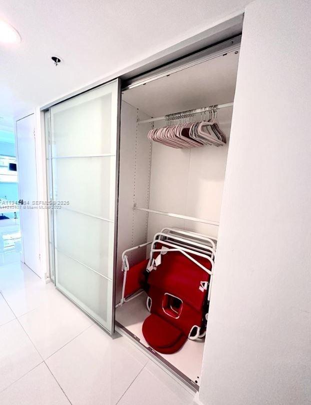A closet with sliding frosted glass doors contains a hanging rod and folded red chairs — 100 Lincoln Rd # 526, Miami Beach FL 33139, MIAMI BEACH, FL