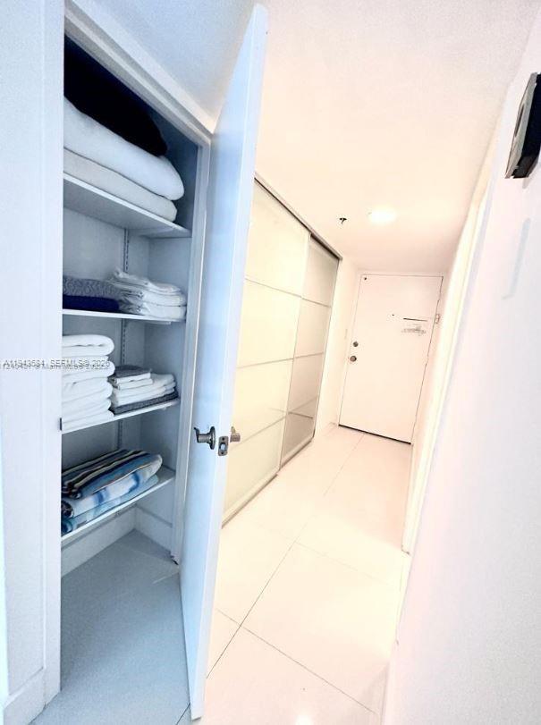 A white hallway features a linen closet with open shelves and a sliding glass door — 100 Lincoln Rd # 526, Miami Beach FL 33139, MIAMI BEACH, FL