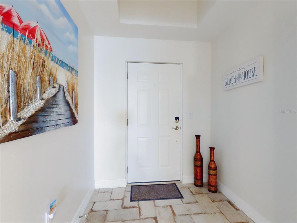 An entryway features a white door, tiled floor, beach-themed wall art, and two decorative vases — 1705 S ATLANTIC AVENUE UNIT 402, NEW SMYRNA BEACH, FL