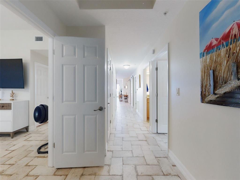 A long hallway with light-colored tile flooring leads toward a bright room in the distance — 1705 S ATLANTIC AVENUE UNIT 402, NEW SMYRNA BEACH, FL