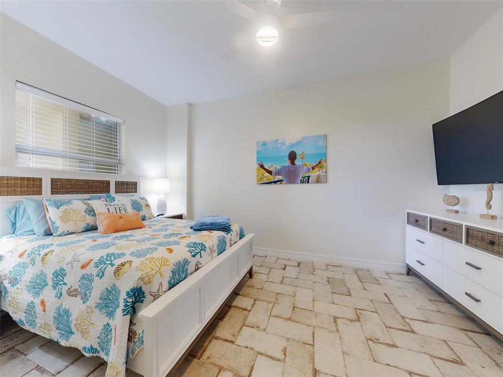 A bedroom features a coral-patterned bedspread, white furniture, and light-colored stone flooring — 1705 S ATLANTIC AVENUE UNIT 402, NEW SMYRNA BEACH, FL