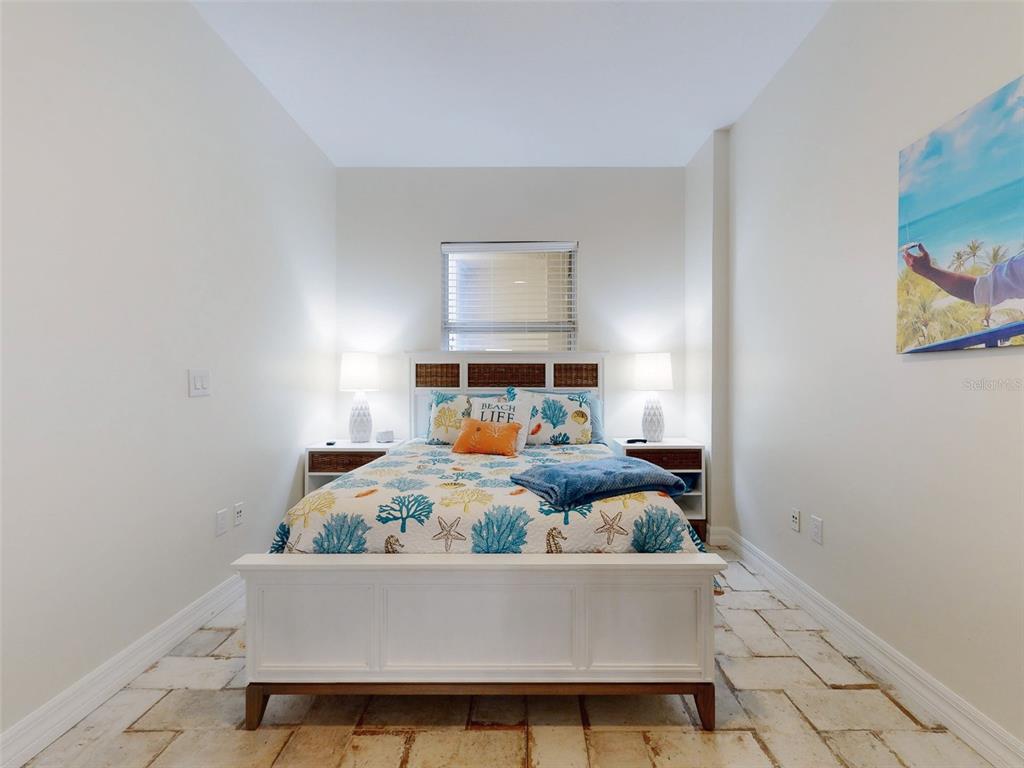 A bedroom features a white bed frame, coastal-themed bedding, and stone tile flooring — 1705 S ATLANTIC AVENUE UNIT 402, NEW SMYRNA BEACH, FL