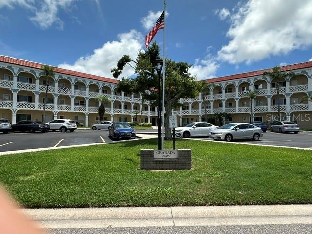 A multi-story apartment building features arched balconies and a central flagpole on a grassy lawn — 2405 FRANCISCAN DRIVE UNIT 23, CLEARWATER, FL