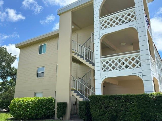 A three-story apartment building features beige siding, open-air stairwells, and decorative white balcony railings — 2405 FRANCISCAN DRIVE UNIT 23, CLEARWATER, FL