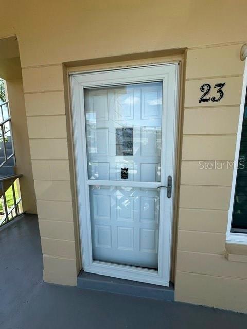 A white storm door with a glass panel is installed on a tan exterior wall — 2405 FRANCISCAN DRIVE UNIT 23, CLEARWATER, FL