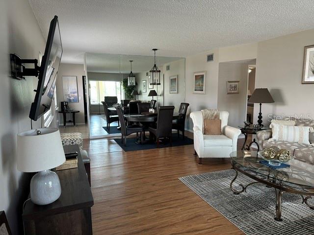 A living room features wood-look flooring, a dining area with a mirrored wall, and furniture — 2405 FRANCISCAN DRIVE UNIT 23, CLEARWATER, FL