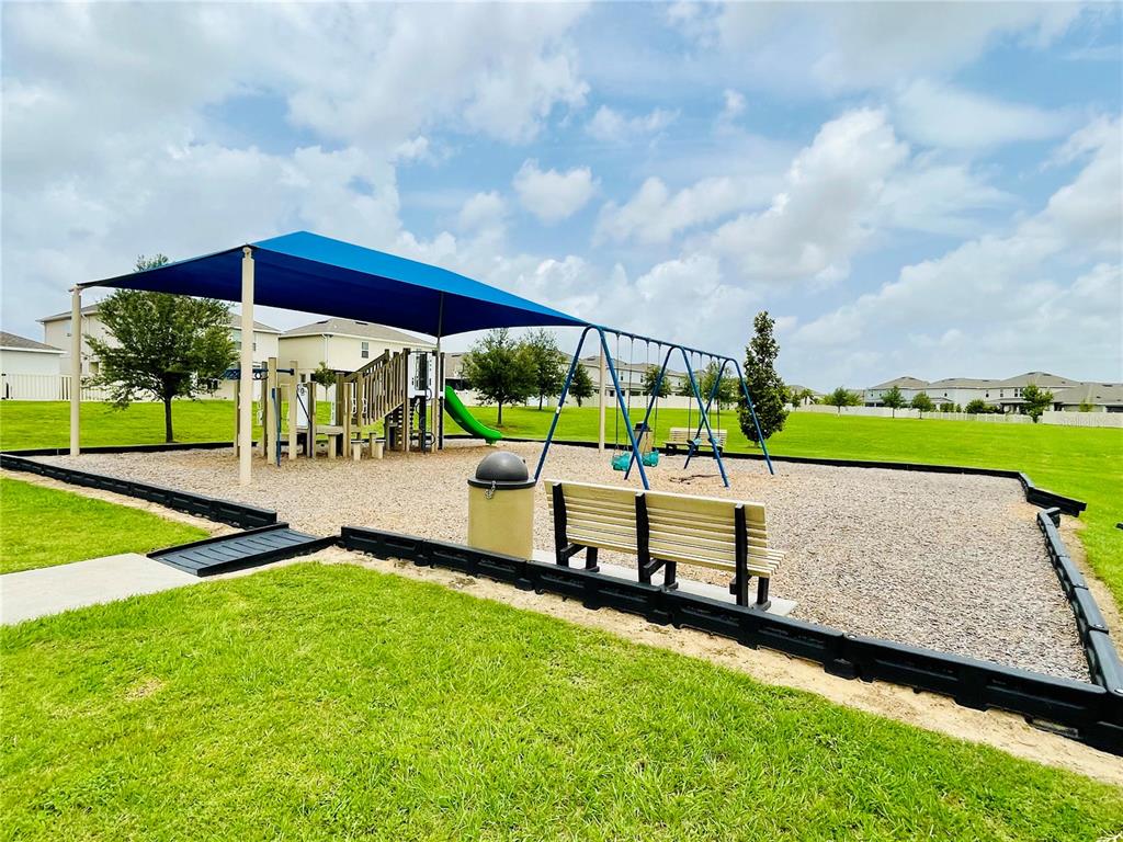 A playground with a blue shade canopy, swing set, and slide on a wood-chipped surface — 367 LEMONGRASS ROAD, MINNEOLA, FL
