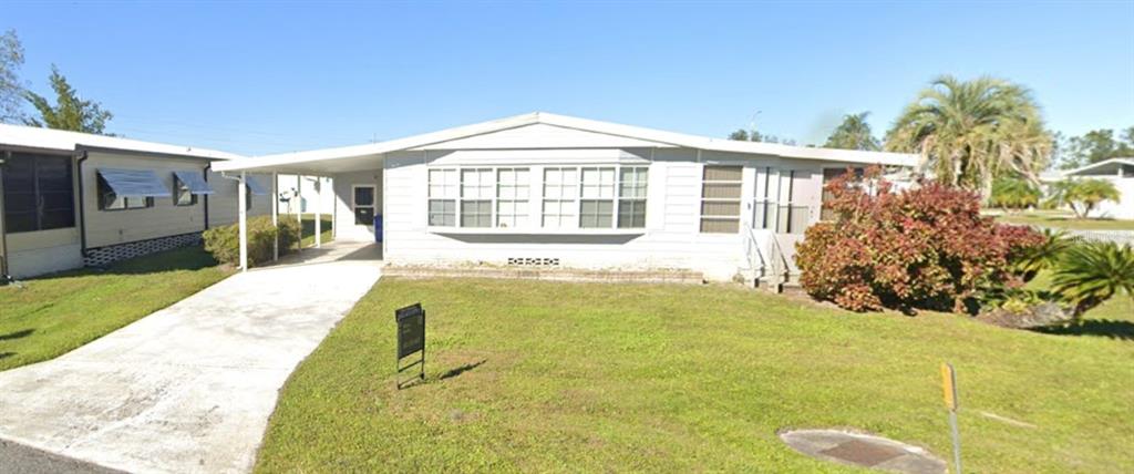 A light-colored manufactured home features a front carport and a large, landscaped yard — 6433 JACARANDA AVENUE NE, WINTER HAVEN, FL